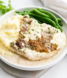 a white plate topped with meat and mashed potatoes covered in gravy next to green beans