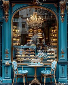 two blue chairs sitting at a table in front of a store window with gold trim