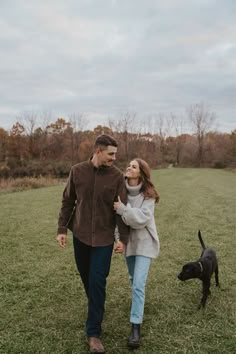 a man and woman walking in the grass with a dog