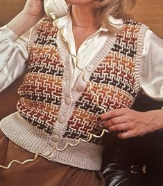 a woman sitting on a couch talking on a cell phone while wearing a knitted vest