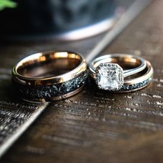 two wedding rings sitting on top of a wooden table next to each other and one has a diamond in the middle