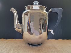 a shiny silver tea pot sitting on top of a burlap cloth covered table