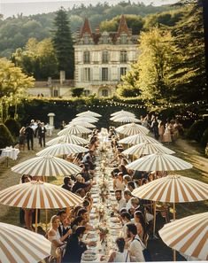 a group of people sitting under umbrellas at a long table in front of a large building