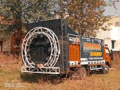 an orange and black truck parked in front of a building with a circular structure on the back