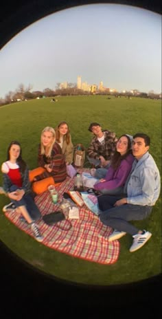 a group of people sitting on top of a blanket in a field next to each other