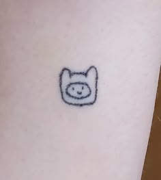 a small tattoo on the leg of a person with a cat face drawn on it