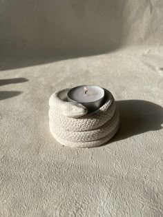 a white candle sitting on top of a pile of rope wrapped around a round object