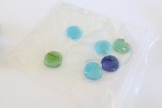 four different colored glass beads on a white surface next to a blue and green object