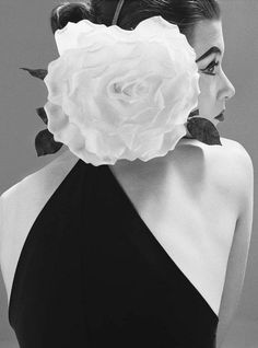 a black and white photo of a woman with a large flower on her back neck