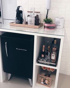 a small refrigerator sitting next to a counter with liquor bottles on it and an icebox