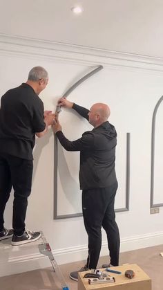 two men are working on an art piece in the middle of a room with white walls