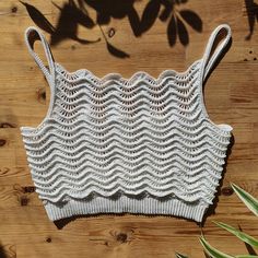 a white crocheted crop top sitting on top of a wooden table next to a plant