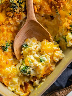 a casserole dish with broccoli and cheese on it, next to a wooden spoon