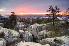 the sun is setting over some rocks and pine trees on top of a mountain range