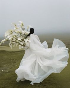 a woman in a white dress holding a bouquet of flowers on top of a grass covered field