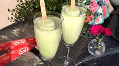 two glasses filled with green liquid sitting on top of a table next to a vase