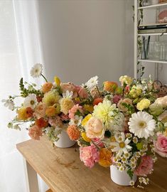 three white vases filled with colorful flowers on a wooden table next to a window