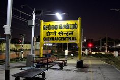 a yellow sign that is on the side of a train track in front of a bench