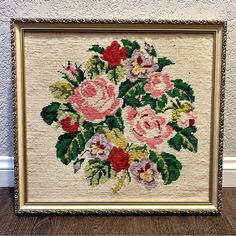 a cross stitch picture frame with flowers in it on a wooden floor next to a wall