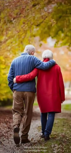 an older couple walking down a path in the fall with their arms around each other