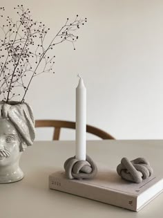 a table with a candle and some kind of sculpture on it, next to a book