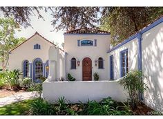 a white house with blue trim and shutters on the front door is surrounded by greenery