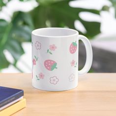 a white coffee mug with strawberries and flowers on it sitting on a wooden table