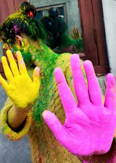 a woman with her hands painted pink and yellow in front of a mirror that is covered in colored powder