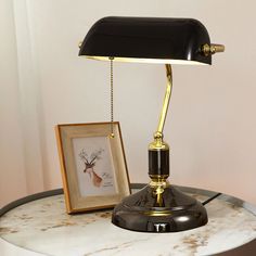 a desk lamp sitting on top of a white table next to a framed picture and an antler's head