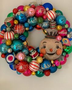 a christmas wreath with ornaments hanging on the wall and a face painted on it's side