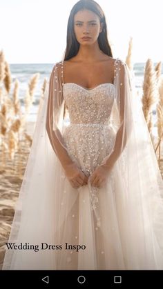 a woman in a wedding dress standing on the beach with her arms behind her back