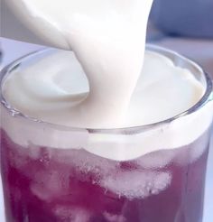 a person pouring milk into a glass filled with ice and cranberry sodas