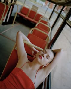 a woman in a red dress sitting on a bus with her arms behind her head