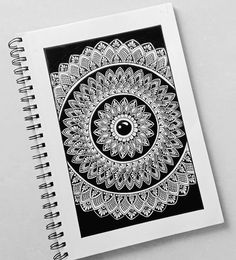 a spiral notebook with an intricate black and white design on the cover, next to a pen