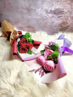 two bouquets of roses are wrapped in pink and purple ribbon on a white furnishing