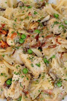 a white plate topped with pasta and meat covered in sauce, peas and seasoning