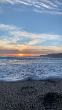 the sun is setting over the ocean with waves coming in to shore and footprints in the sand