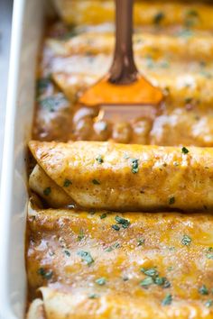 an enchilada in a white casserole dish with a spatula