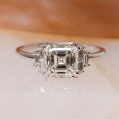 an emerald cut diamond ring sitting on top of a table