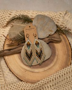 a pair of earrings sitting on top of a piece of wood next to a rock