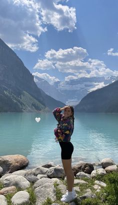 a woman standing in front of a mountain lake