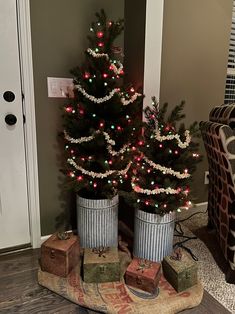 two small christmas trees sitting in buckets on the floor next to each other with presents under them