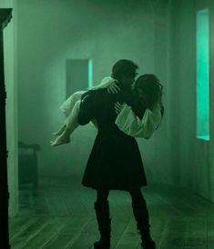 a man holding a woman in the middle of a room with green light coming from behind