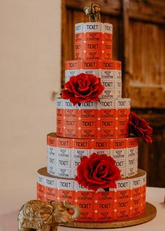 a three tiered cake with red roses on top and tickets around the bottom layer