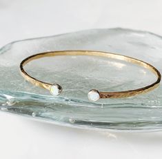 This gorgeous cuff is stunning worn on its own or can be mixed with other bangles and bracelets. It features two lab created 4mm opal cabochons bezel set into a sterling silver tube setting. The cuff is hand forged from heavy gauge 14kt goldfill wire and hammered with the dappled texture to catch the light. It sits comfortably on the wrist and is adjustable to fit most any wrist. Luxury Hammered Minimalist Bracelets, Luxury Minimalist Hammered Bracelets, Opal Cuff Bracelet, Davidson Nc, Bangles And Bracelets, Opal Gifts, Silversmith Jewellery, Hammered Gold, Gold Cuffs