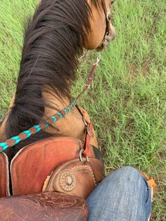 a brown horse standing on top of a lush green field next to a person wearing boots