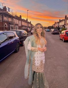 a woman standing on the side of a road in front of parked cars at sunset