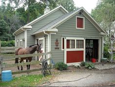 a brown horse standing in front of a gray house with red doors and windows on it's side