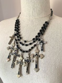 "Beautiful vintage silver cross spiritual statement necklace. This beautiful necklace features a collection of vintage silver & black crosses from France. The crosses hang from a cascade of vintage French black rosary chains. The rosary beads are made from wood. The large crosses are silver plated and are stamped Souvenir de Lourdes on the back. Overall necklace length is adjustable from 17-1/2\" to 21-1/2\", with a cross dangling from the end. The center  drapes down 4\". It fastens with a silv Luxury Crucifix Necklace As Gift, Black Beaded Crucifix Jewelry, Silver Crucifix Jewelry With Black Beads, Black Crucifix Jewelry For Jewelry Making, Silver Rosary With Black Beads And Crucifix, Handmade Black Crucifix Necklace, Handmade Black Cross Necklace, Handmade Black Cross Pendant Necklace, Vintage Black Cross Necklace