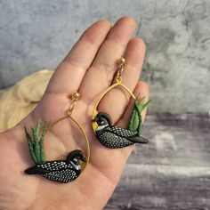 a hand holding two earrings with birds on them